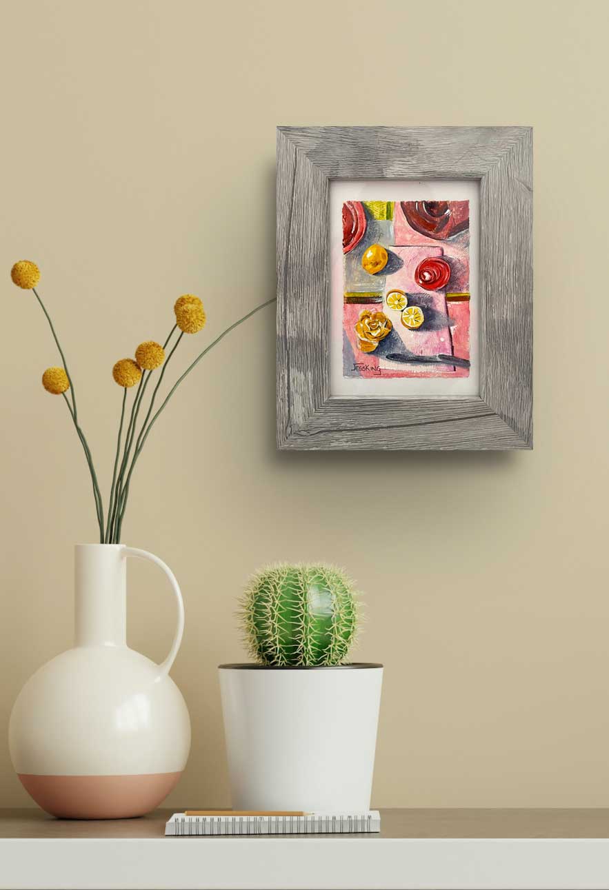 Framed original artwork on a wall of a lemon, flower and vase in reds and yellows.
